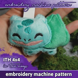 Könnte beinhalten: Ein grünes und blaues Plüschtier eines Comic-Charakters mit einem lächelnden Gesicht. Das Spielzeug ist mit Details bestickt und mit "ITH 4x4 in the hoop embroidery machine pattern" beschriftet.