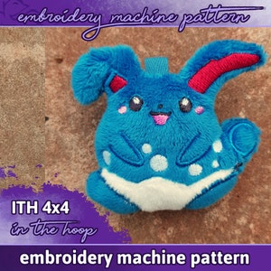 May include: A blue and white plush toy in the shape of a cartoon character with large ears and a smiling face. The toy is designed for embroidery machine use and is labelled "ITH 4x4 in the hoop embroidery machine pattern".