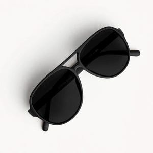 May include: Matte black aviator sunglasses featuring a double bridge design and dark, solid lenses. The frame has a smooth, non-reflective finish with a distinct brow bar connecting the two rounded lens rims, providing a classic, uniform look.
