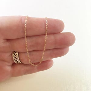 May include: A delicate gold-colored chain necklace. The chain is held in a hand, showcasing its fine links and subtle shine. The necklace is a simple, elegant piece of jewelry.