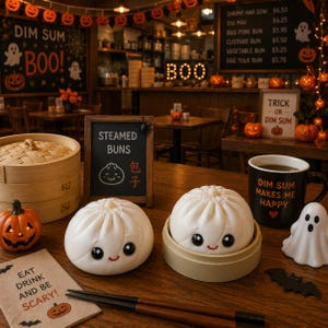 May include: Two white steamed buns with smiling faces, one resting in a small bamboo steamer base, accompanied by a black mug with the text "DIM SUM MAKES ME HAPPY," a small orange jack-o'-lantern, a ghost figurine, and a pair of dark chopsticks.