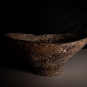 May include: A handcrafted, brown, textured bowl with an unusual, asymmetrical shape. The bowl has a rough, earthy appearance, with variations in colour and texture. The interior is smooth, while the exterior has a rugged, natural feel. This decorative bowl is perfect for displaying items.