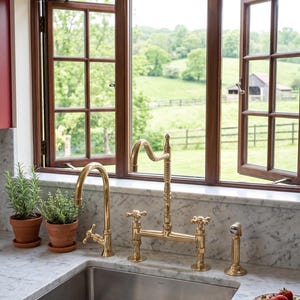 May include: A kitchen sink with a gold faucet and a window overlooking a green landscape. The sink is set in a marble countertop, with potted herbs and a plate of strawberries nearby. A vintage-style light fixture is mounted above the window.