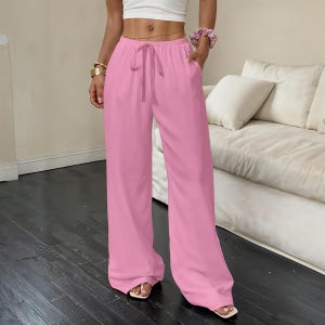 May include: Solid pink wide-leg trousers featuring a high-rise elastic waistband with a matching drawstring tie. These loose-fitting pants include side pockets and fall to a full-length hem, providing a relaxed silhouette and a clean, minimalist look.