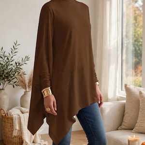 May include: A brown long-sleeve tunic with a high turtleneck collar, featuring an asymmetrical hemline that drapes longer on the sides. The garment is paired with blue denim jeans, creating a layered look with a loose, flowing silhouette.