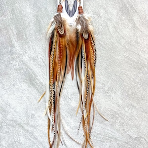 May include: A pair of long, brown, white, and black feather earrings with leather tassels. The earrings are on a card that says "Fringed in Faith".
