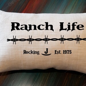 May include: A white pillow with black text that reads "Ranch Life" with a barbed wire design and "Rocking J Est. 1975" below.