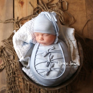 May include: A newborn baby is swaddled in a light blue fabric with bows and wearing a matching light blue hat. The baby is lying in a wooden bowl on a rustic background. The text "Home Sewn photography props" is visible in the image.
