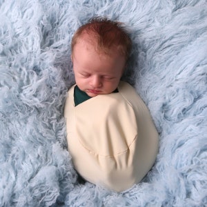 May include: A newborn baby is sleeping peacefully in a white swaddle on a light blue fluffy blanket.