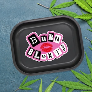 May include: Black rectangular rolling tray with rounded corners. The tray features a pink and white graphic with the words "BURN BLUNTS" and a red lip design. Green cannabis leaves are in the background.