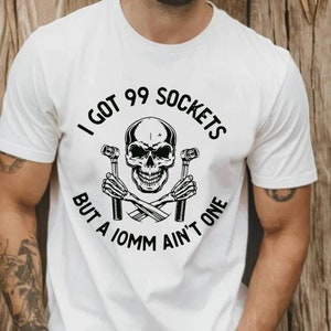 Puede incluir: Camiseta blanca con un cráneo negro y llaves cruzadas. El texto dice "Tengo 99 enchufes pero un 10 mm no es uno."