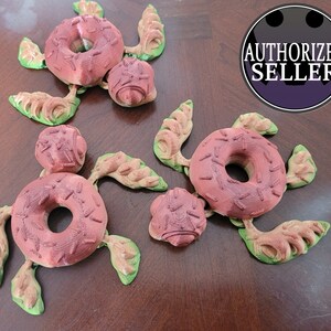 May include: Several 3D-printed turtle figurines with a donut-shaped shell and a small ball for the head. The turtles are primarily reddish-brown with green and tan accents. The image also includes an "AUTHORIZED SELLER" logo.