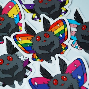 May include: A collection of stickers featuring a cartoon moth with a fluffy gray body, red eyes, and black antennae. The moth's wings display various pride flag designs, including rainbow, transgender, and bisexual flags. The stickers have a white border.