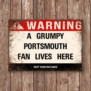 Może przedstawiać: Rdzewiejący metalowy znak z czerwonym trójkątem ostrzegawczym i tekstem "WARNING A GRUMPY PORTSMOUTH FAN LIVES HERE KEEP YOUR DISTANCE".