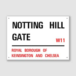 May include: White sign with black text that reads "Notting Hill Gate" and "Royal Borough of Kensington and Chelsea". The sign also has the postal code "W11" in black text.