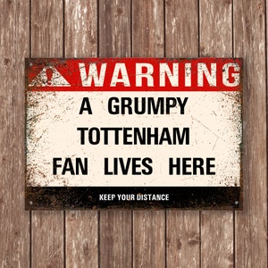 Peut inclure: Un panneau d'avertissement avec un fond rouge et du texte noir qui dit "WARNING A GRUMPY TOTTENHAM FAN LIVES HERE KEEP YOUR DISTANCE". Le panneau est conçu pour ressembler à du métal vieilli.