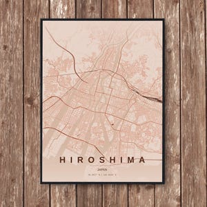 Puede incluir: Una impresión enmarcada del mapa de Hiroshima, Japón, en un esquema de color melocotón y marrón apagado. El mapa de la ciudad presenta diseños de calles detallados y características geográficas. La palabra "HIROSHIMA" está impresa en negrita en la parte inferior, con "JAPAN" y coordenadas.