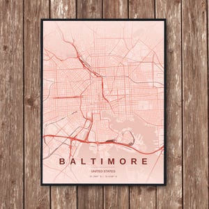May include: A framed map print of Baltimore, Maryland, in the United States. The map shows a network of roads and streets in shades of red against a light pink background. The city name and country are printed in a dark red font.