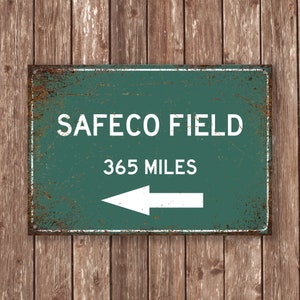 May include: A vintage-style metal sign with a green background and white text. The sign reads "SAFECO FIELD 365 MILES" with a white arrow pointing to the left.