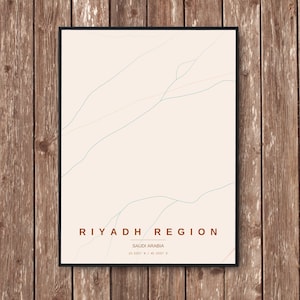 Op de afbeelding: Een ingelijste kunstdruk met een minimalistisch kaartontwerp van de regio Riyad in Saoedi-Arabië. Het kunstwerk heeft een crèmekleurige achtergrond met subtiele, vloeiende lijnen in groen en perzik. De tekst "RIYADH REGION" en "SAUDI ARABIA" wordt in een bruin lettertype weergegeven.