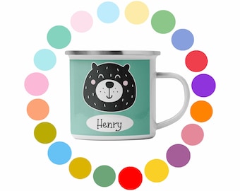 Könnte beinhalten: Weißer Emaillebecher mit türkisem Hintergrund und einer Illustration eines schwarzen Bären. Der Bär hat rosa Wangen und eine weiße Schnauze. Der Name "Henry" ist weiß auf einem Oval gedruckt. Ein Kreis aus bunten Punkten umgibt die Tasse.