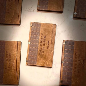Puede incluir: Cinco cubiertas de menú de madera con el texto "The Purty Kitchen" y "Est. 1728" en ellas.