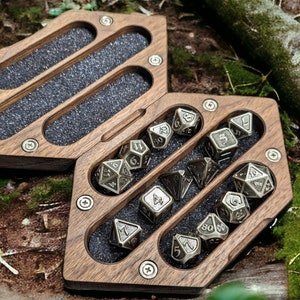 May include: A wooden box with a hinged lid, open to reveal a set of 12 silver metal dice. The dice are arranged in rows within the box, with each die showing a different number.