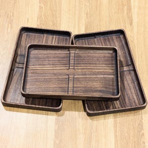 May include: Three wooden serving trays, one with four compartments, stacked on top of each other. The trays are dark brown and have a wood grain pattern.