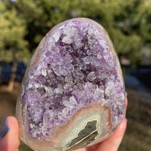 May include: A large, purple amethyst geode with a clear, crystal-like exterior. The geode is filled with small, purple crystals and has a natural, rough texture.