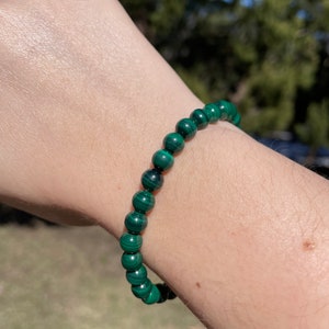 May include: A green malachite beaded bracelet. The bracelet is made of round beads with a dark green and light green marbled pattern.