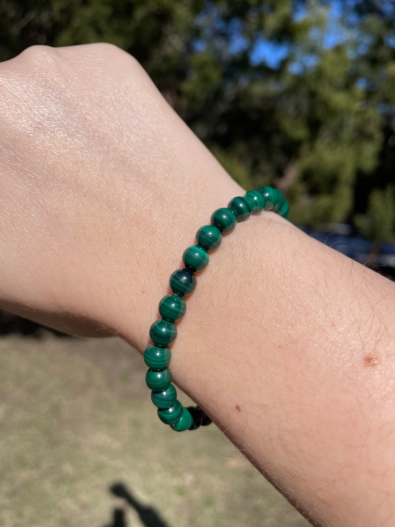 May include: A green malachite beaded bracelet. The bracelet is made of round beads with a dark green and light green marbled pattern.