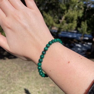 May include: A green malachite beaded bracelet on a person's wrist.