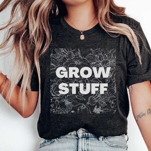 May include: A dark gray t-shirt with a white floral design and the text "GROW STUFF" in white.