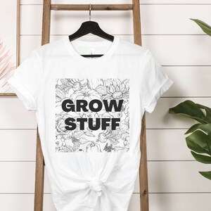 May include: White t-shirt with a black and white floral design and the text "GROW STUFF" printed on the front.