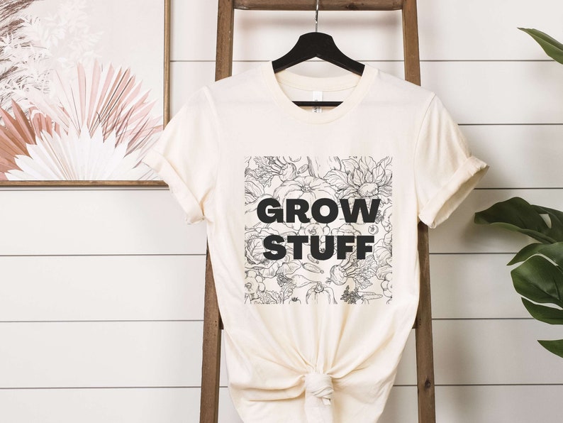 May include: A cream colored t-shirt with a black and white floral design and the text "GROW STUFF" printed on the front.