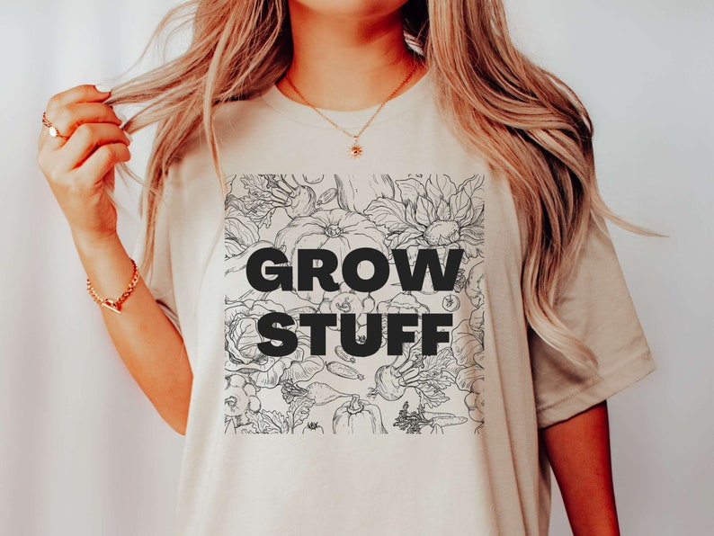 May include: A beige t-shirt with a black and white graphic of vegetables and flowers. The graphic includes the text "GROW STUFF".