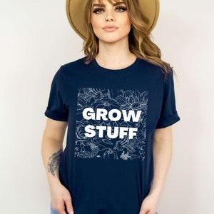May include: A navy blue t-shirt with a white floral design and the text "GROW STUFF" in white.