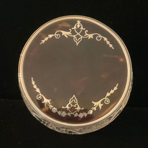 Peut inclure: Une boîte à bijoux ronde en verre transparent avec un intérieur en écaille de tortue brune. Le couvercle est décoré de motifs floraux en filigrane argenté.