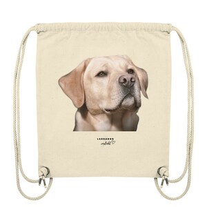 May include: A beige drawstring bag with a picture of a golden labrador retriever's head on the front. The text "LABRADOR verliebt" is printed below the image with a small heart symbol.