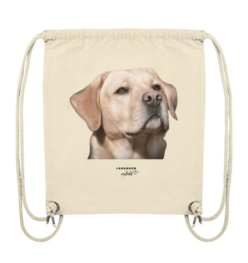 May include: A beige drawstring bag with a picture of a golden labrador retriever's head on the front. The text "LABRADOR verliebt" is printed below the image with a small heart symbol.
