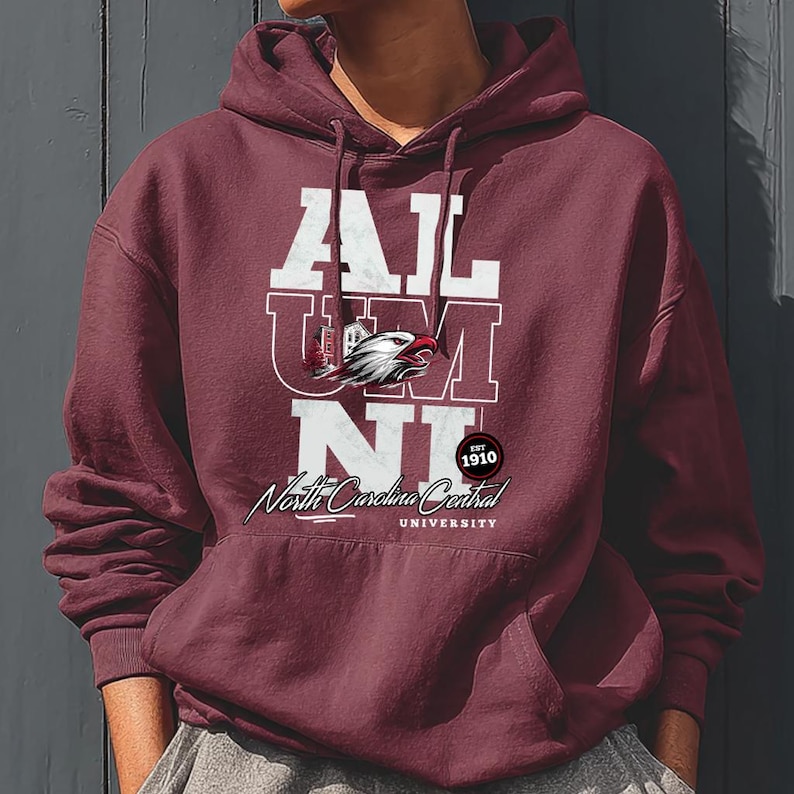 May include: A maroon hoodie with the text "ALUMNI" in white block letters. Below the text is a graphic of an eagle and the words "North Carolina Central University" in a script font. The hoodie also has a pocket.