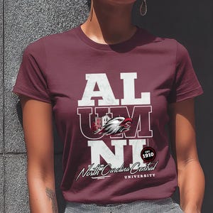 May include: Maroon t-shirt with the word "ALUMNI" in white block letters. The "U" and "M" are partially overlaid with a graphic of a building and an eagle head. Below is "North Carolina Central University" in script.