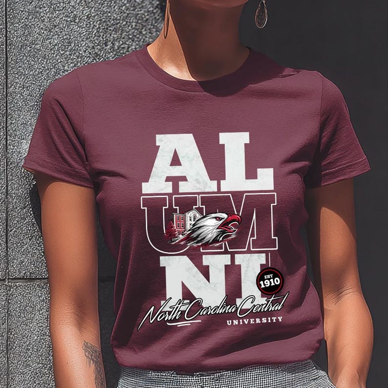 May include: Maroon t-shirt with the word "ALUMNI" in white block letters. The "U" and "M" are partially overlaid with a graphic of a building and an eagle head. Below is "North Carolina Central University" in script.