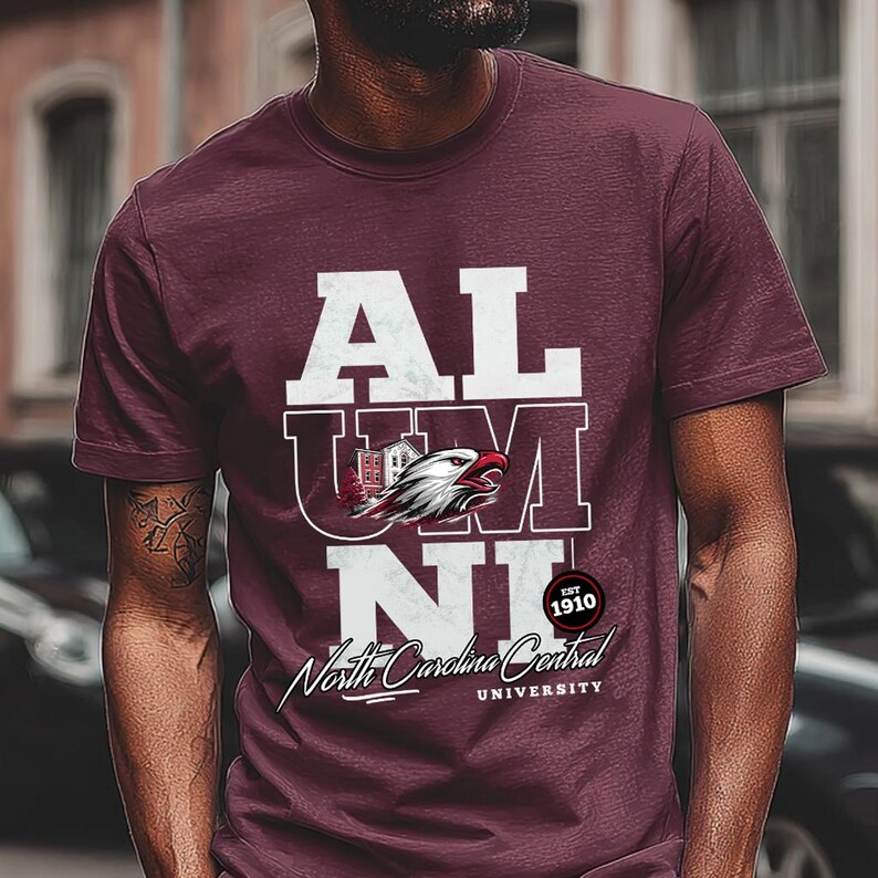 May include: Maroon t-shirt with white text that reads "ALUMNI" stacked vertically. The "U" features a graphic of an eagle and a building. Below the text is "North Carolina Central University" and "EST 1910".