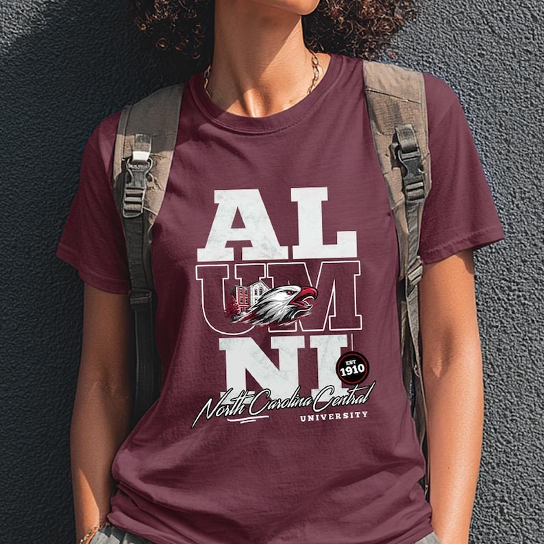 May include: Maroon t-shirt with the word "ALUMNI" in white block letters. The "U" and "M" have a graphic of a building and an eagle. Below is "North Carolina Central University" in script. Established 1910.