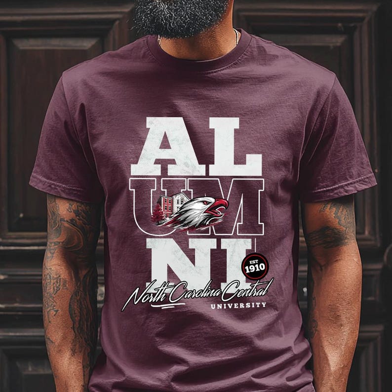 May include: Maroon t-shirt with the word "ALUMNI" in white block letters. The shirt features a graphic of an eagle and the text "North Carolina Central University" in a script font. The year "1910" is also printed on the shirt.
