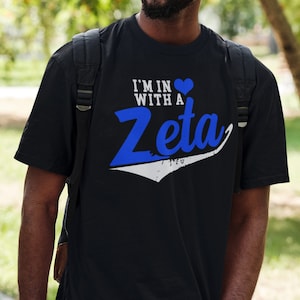 May include: Black t-shirt with a white and blue graphic that says "I'm in with a Zeta" and a blue heart.