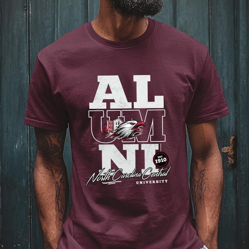 May include: Maroon t-shirt with the word "ALUMNI" in white block letters. The shirt features a graphic of an eagle and the text "North Carolina Central University" in script. The year "1910" is also displayed.