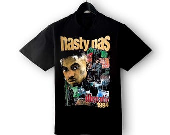 May include: Black t-shirt featuring a graphic of the rapper Nas. The design includes the text "nasty nas" in gold lettering above a portrait of the artist. Below the portrait is the text "illmatic 1994".