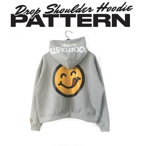 Könnte beinhalten: Grauer Kapuzenpullover mit überschnittenen Schultern und einem großen gelben Smiley-Gesicht auf dem Rücken. Der Hoodie hat den Text "Drop Shoulder Hoodie Pattern" darüber und "SOODTASTE MARKET" auf der Kapuze.